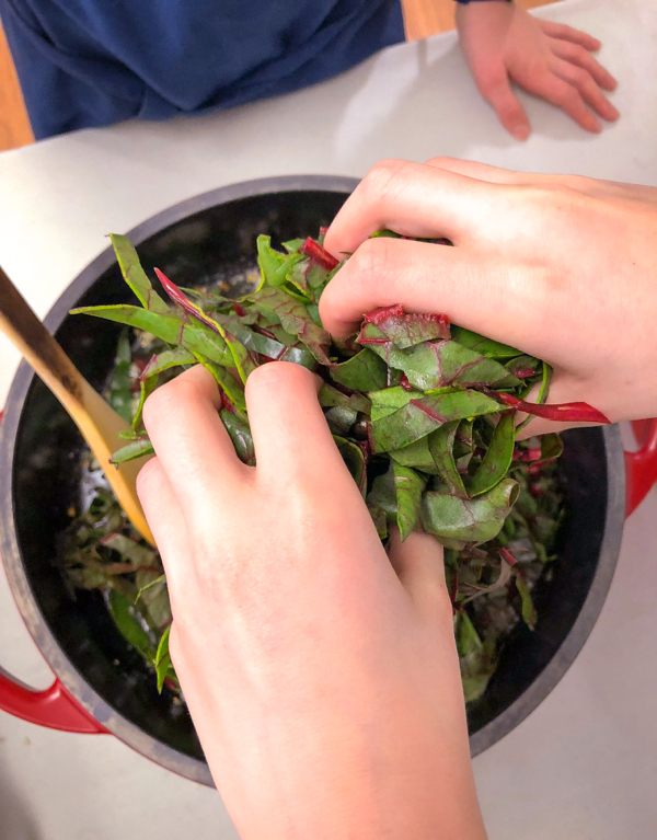Kids adding chard to frying pan for Orecchiette Pasta with Chard from Bringing it Home on eatlivetravelwrite.com