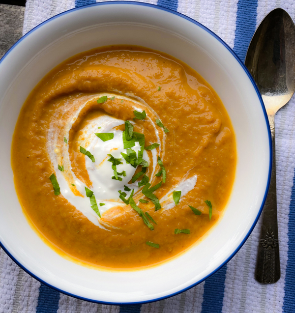 Curried coconut carrot and pumpkin soup in a bowl on a blue and white napkin