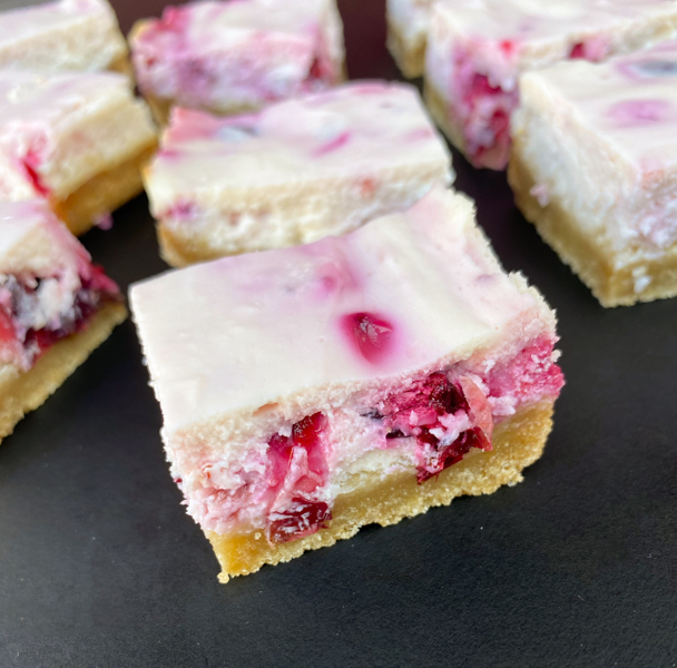 Cranberry Swirl Cheesecake Bars on a black serving board