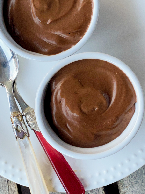 Two dark chocolate puddings in white ramekins with small spoons.