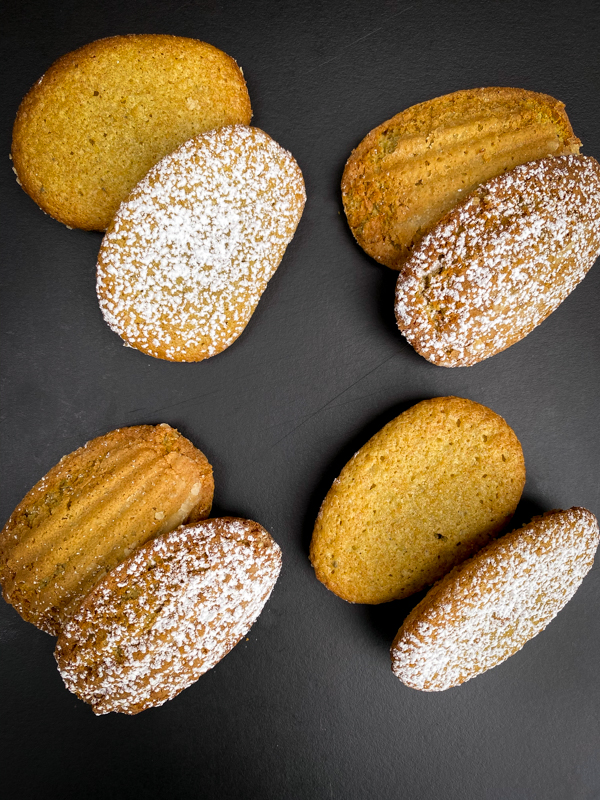 Matcha white chocolate madeleines dusted with icing sugar on a black tray.