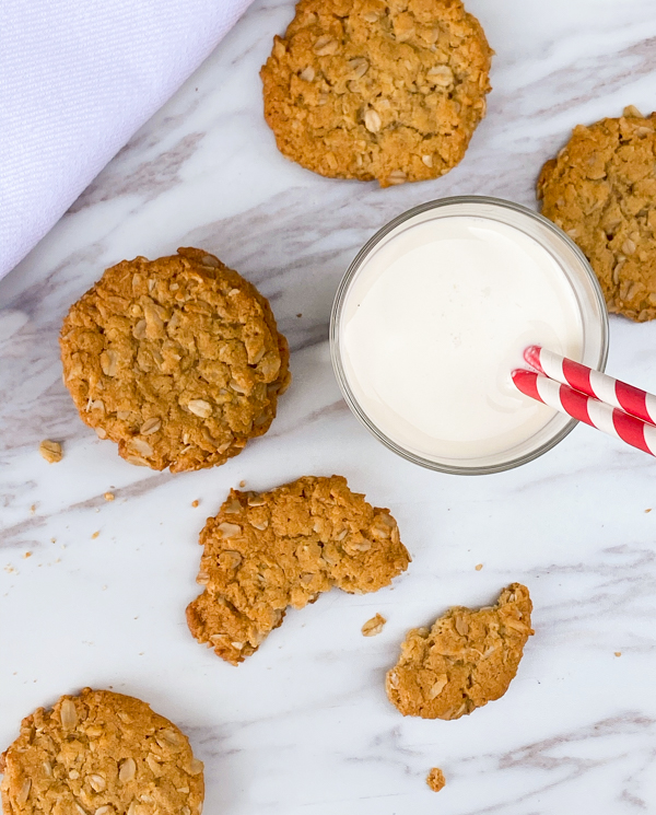 Gluten-free vegan ANZAC biscuits on a marble surface with a glass of milk.