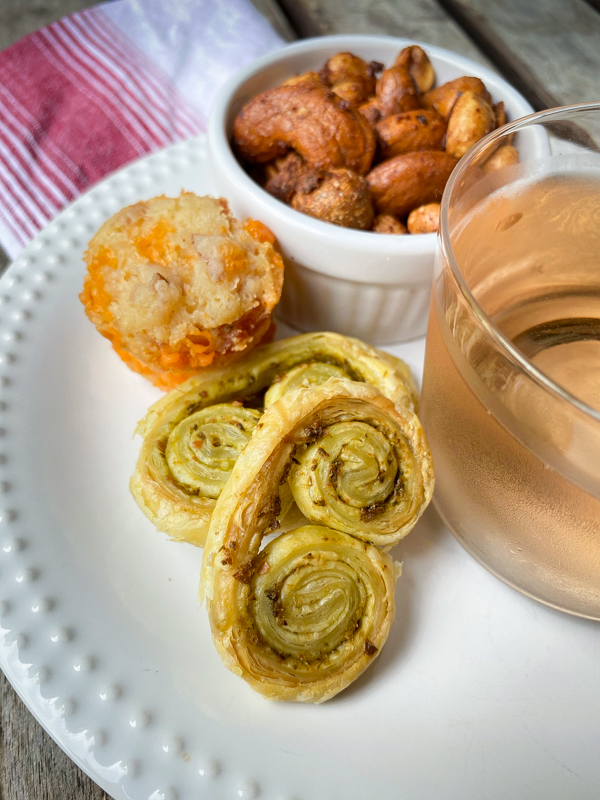 A selection of cocktail snacks with a glass or rosé on a white plate with a red and white napkin.