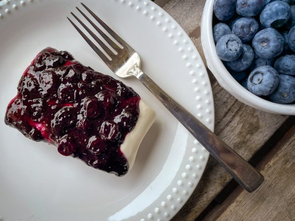 Overhead view of Blueberry cheesecake bar on a plate with a bowl of blueberries next to it.