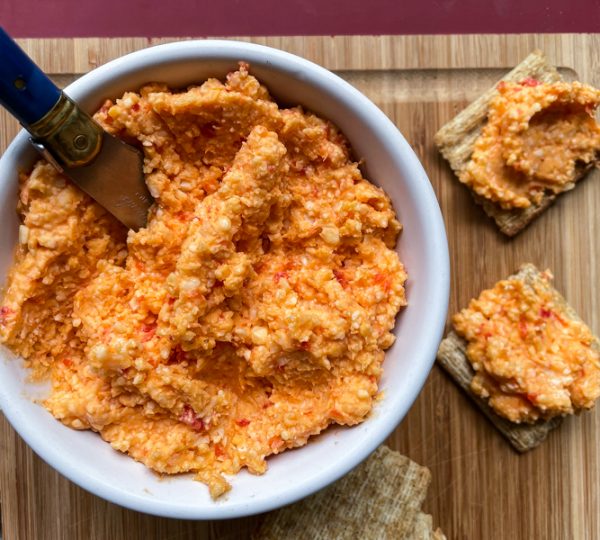 Dorie Greenspan's Pimento Cheese in a white bowl and spread on some crackers on a cutting board.