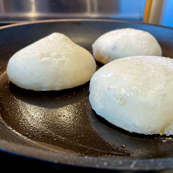 English muffins cooking in a buttered skillet.
