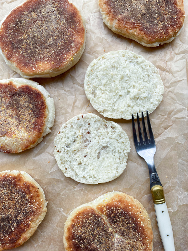 Dorie Greenspan English muffins on a baking tray with one split open.