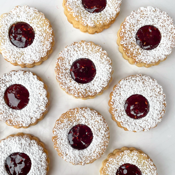 Linzer cookies dusted with icing sugar on a white plate.