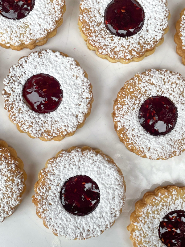 Jam-filled linzer cookies on a white plate.