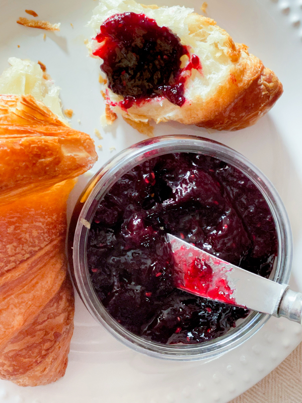 Mulled wine jam in a pot with a croissant on a plate.