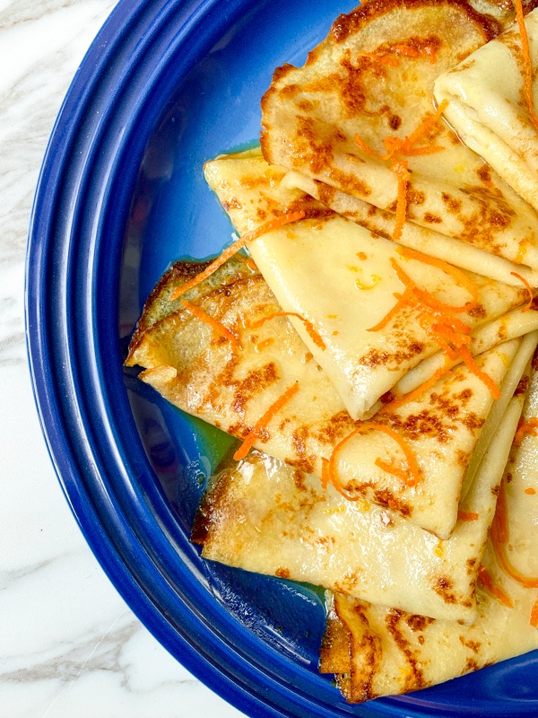 Close up of Crepes Suzette on a blue plate with strips of orange zest on top.