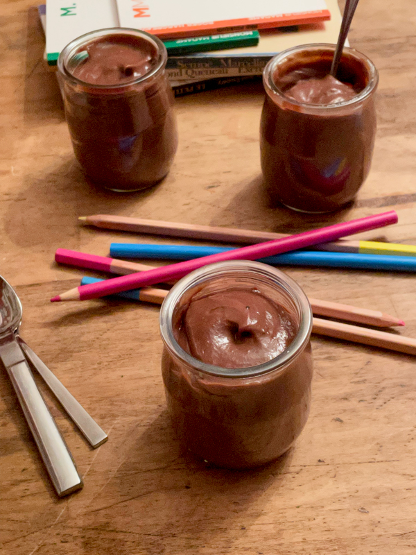 Little Nutella puddings on a wooden surface with coloured pencils.