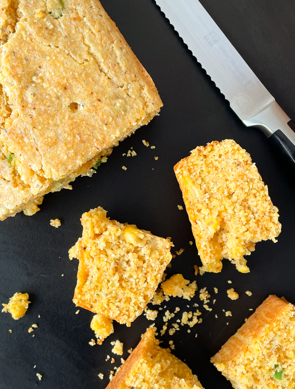Pieces of Whip-It-Up-Quick Cornbread from Baking with Dorie on a black serving tray with a knife next to it.