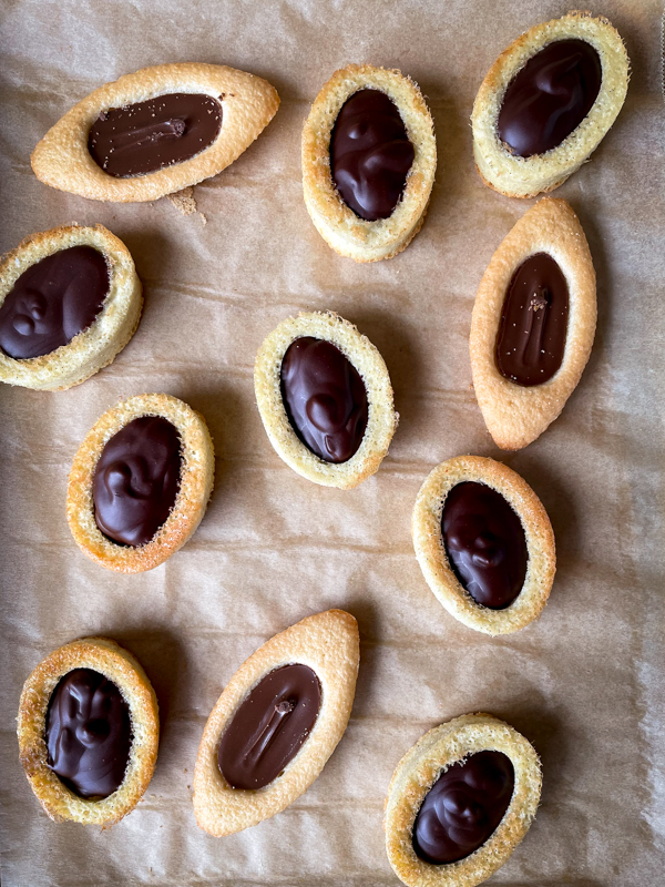 Homemade and store-bought chocolate barquette cookies on a baking tray lined with parchment.