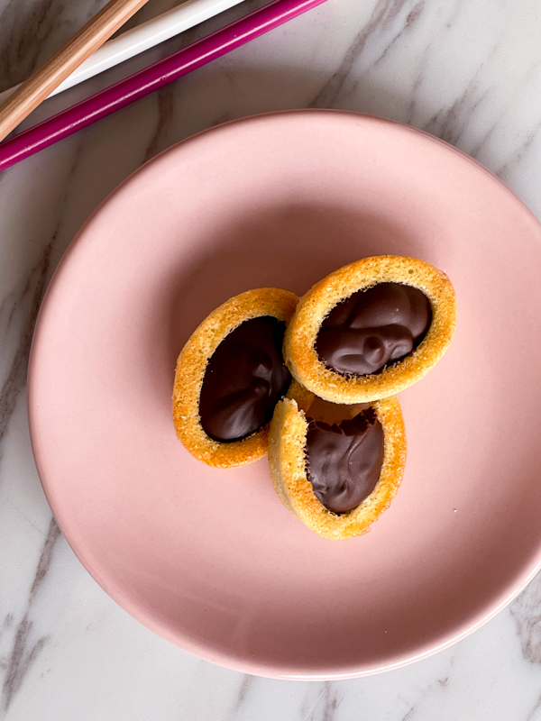 Three chocolate barquette cookies on a pink plate with coloured crayons next to the plate..
