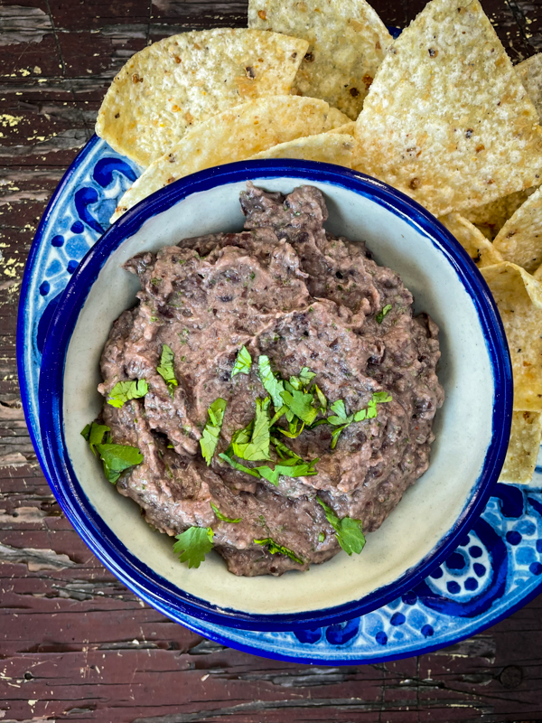 Black bean-chipotle dip in a blue bowl with corn chips on the side.