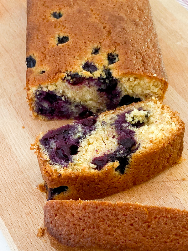 Cornmeal-buttermilk loaf cake from Everyday Dorie with blueberries, sliced on a cutting board.
