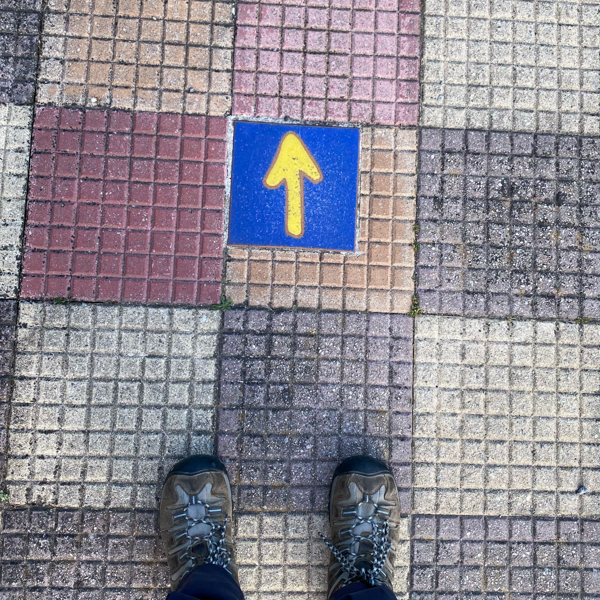 Feet next to a Camino de Santiago marker in Portomarín.