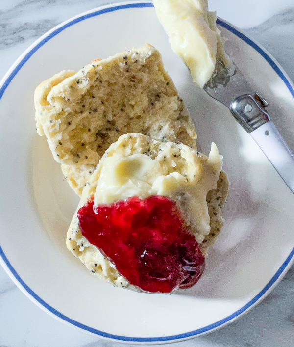 Lemon poppyseed buttermilk scones with butter and jam on a plate with a butter knife.