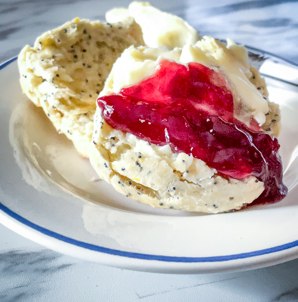 A lemon and poppyseed scone with butter and jam on a white and blue plate.