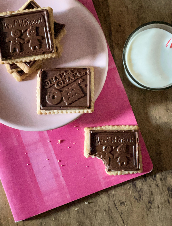 A plate of homemade petit écolier cookies on a pink notebook with a glass of milk next to it.