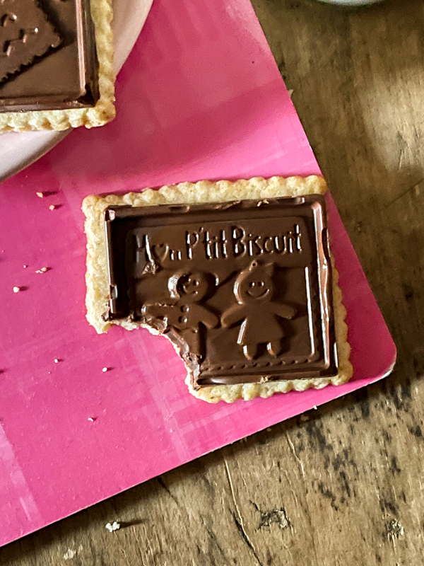 A homemade petit écolier cookie on a pink notebook with a bite taken out of the cookie.