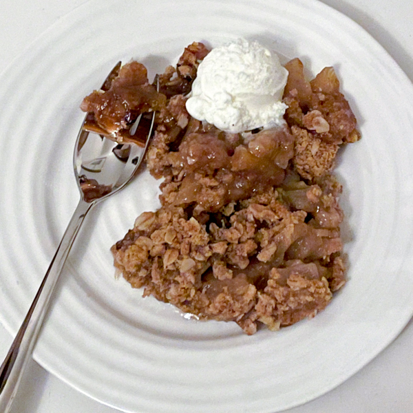 A slice of Caramel-Apple Crisp in a white bowl with a scoop of ice cream on top.