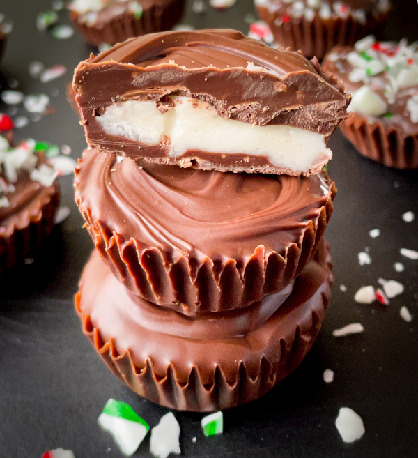 Chocolate peppermint creme cups on a black cutting board with crushed candy cane scattered around.