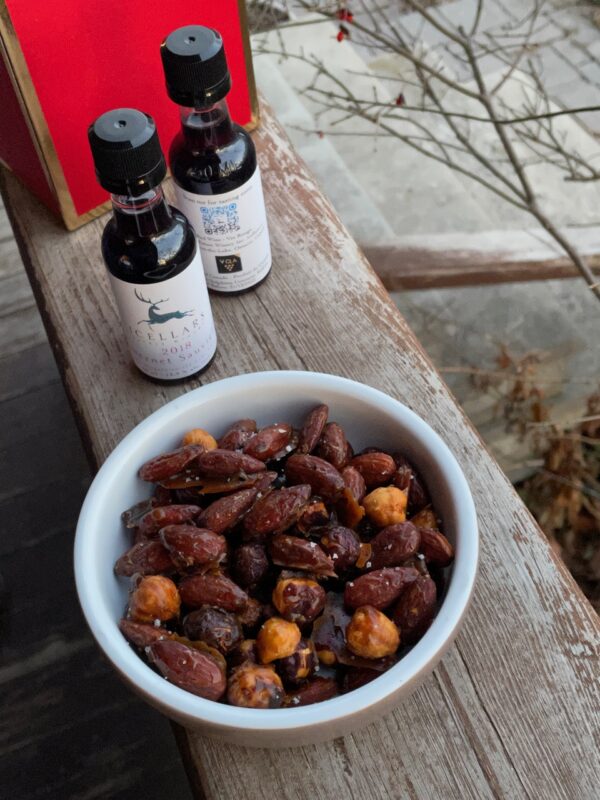 Candied Cocktail Nuts from Everyday Dorie in a small dish on a wooden ledge with two small bottles of wine behind it..