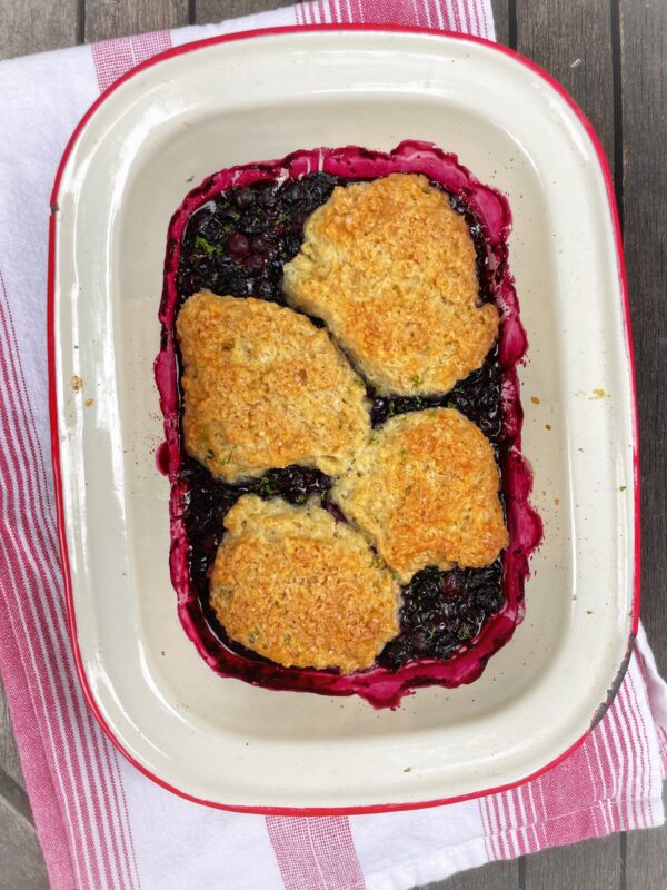 Dorie Greenspan's Cottage Berry Cobbler in a white and red enamel dish on a red and white tea towel.