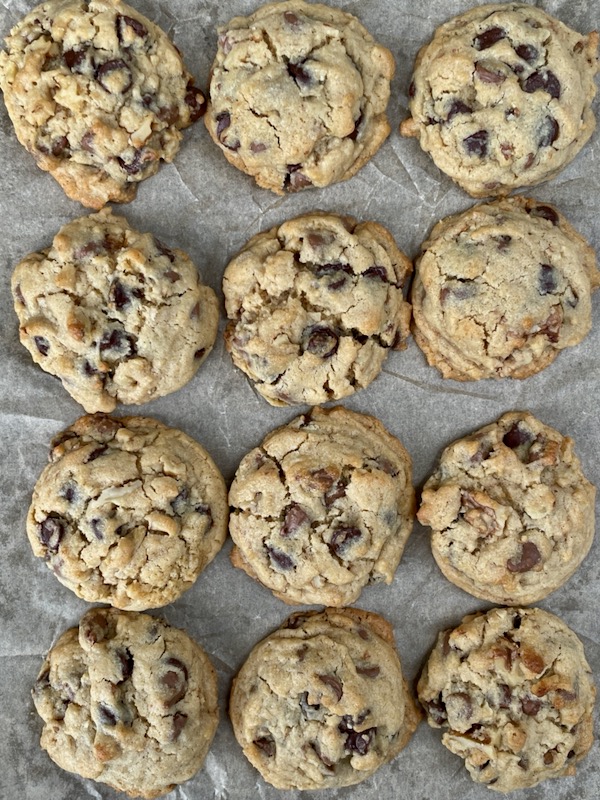 Classic Choc Bit Biscuits (Chocolate Chip Cookies) on a parchment=lined baking tray.