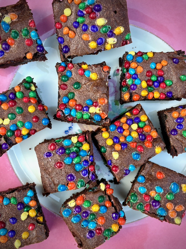 Brownies topped with colorful candy-coated chocolates arranged in squares on a plate. (Rainbow M&M-like toppings)