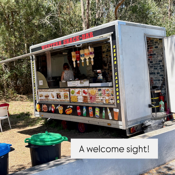Mobile snack bar truck serving ice cream and drinks, with cones displayed and a customer at the counter.