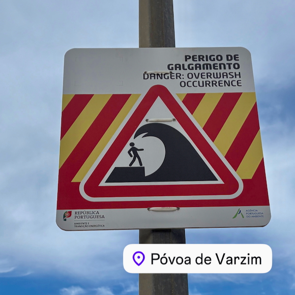 Warning sign: person on a wave inside a red triangle; text reads 'Perigo de alagamento' ('Danger: Overwash Occurrence'); Póvoa de Varzim label at bottom.