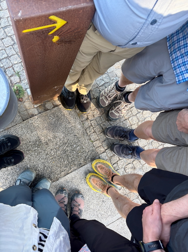 Top-down view of a group standing in a circle, feet around a brown metal post with a yellow arrow marker on it.