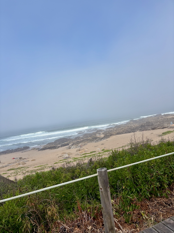 Coastal beach with a rocky shoreline, waves breaking along the coast, under a blue sky.