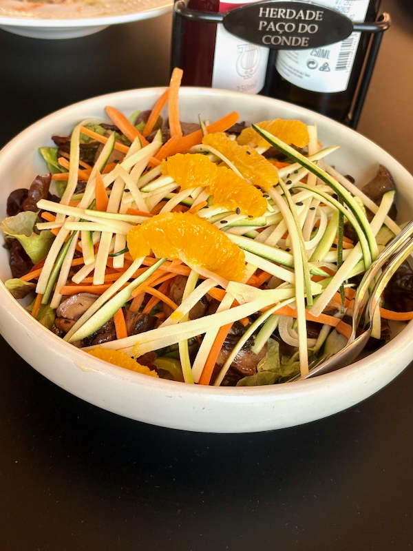 Bowl of mixed salad with zucchini ribbons, carrot sticks, orange segments, lettuce, and mushrooms.