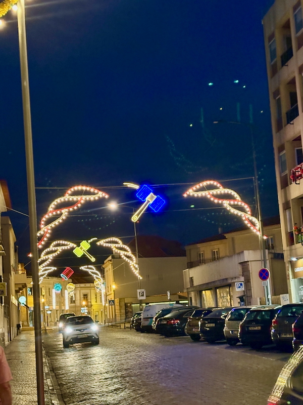 Night street at dusk with festive neon arches shaped like hammers across the road; a large blue neon hammer hangs above the center while cars line both sides.