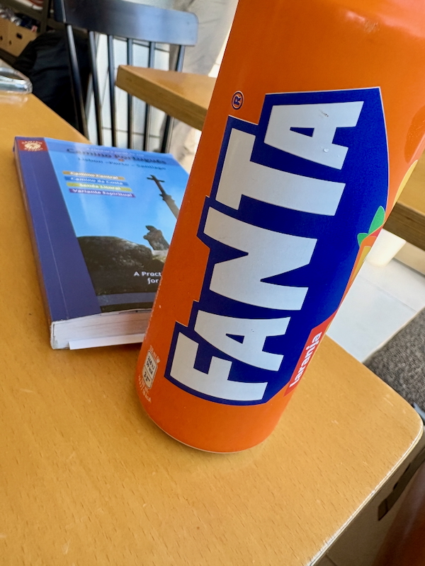 Orange Fanta bottle leaning on a desk with a blue textbook in the background.