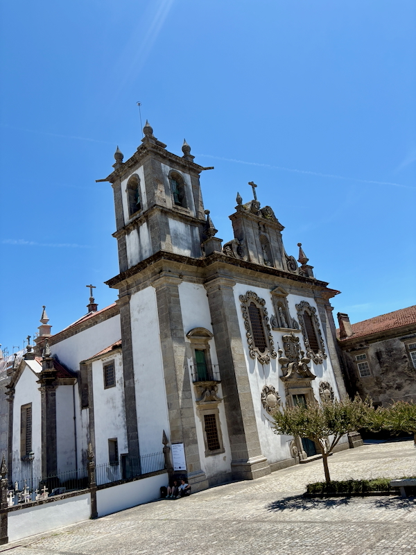 Baroque-style church with ornate facade and twin bell towers under a clear blue sky in a sunny plaza.