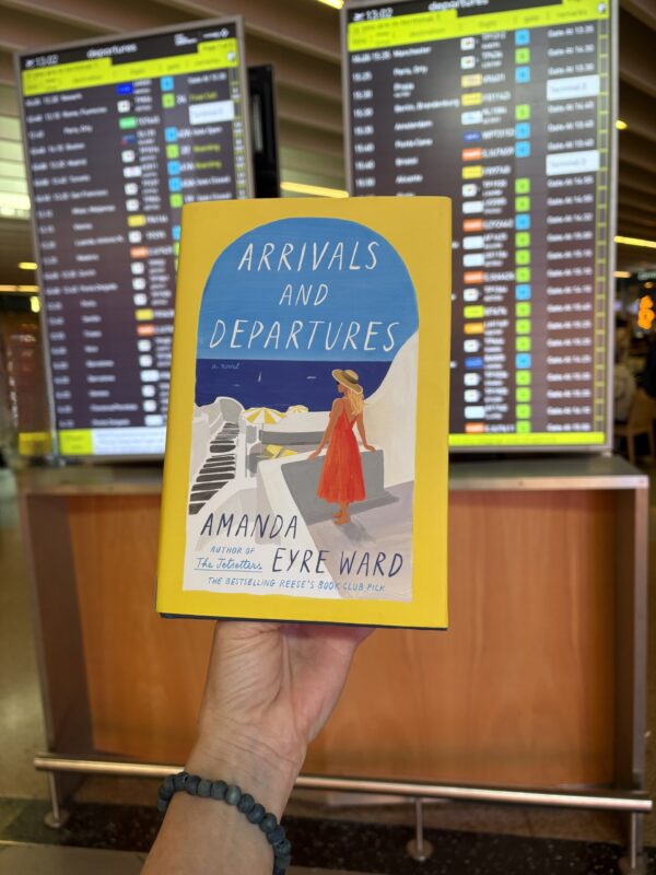 Amanda Eyre Ward Arrivals and Departures book in front of an airline departures board