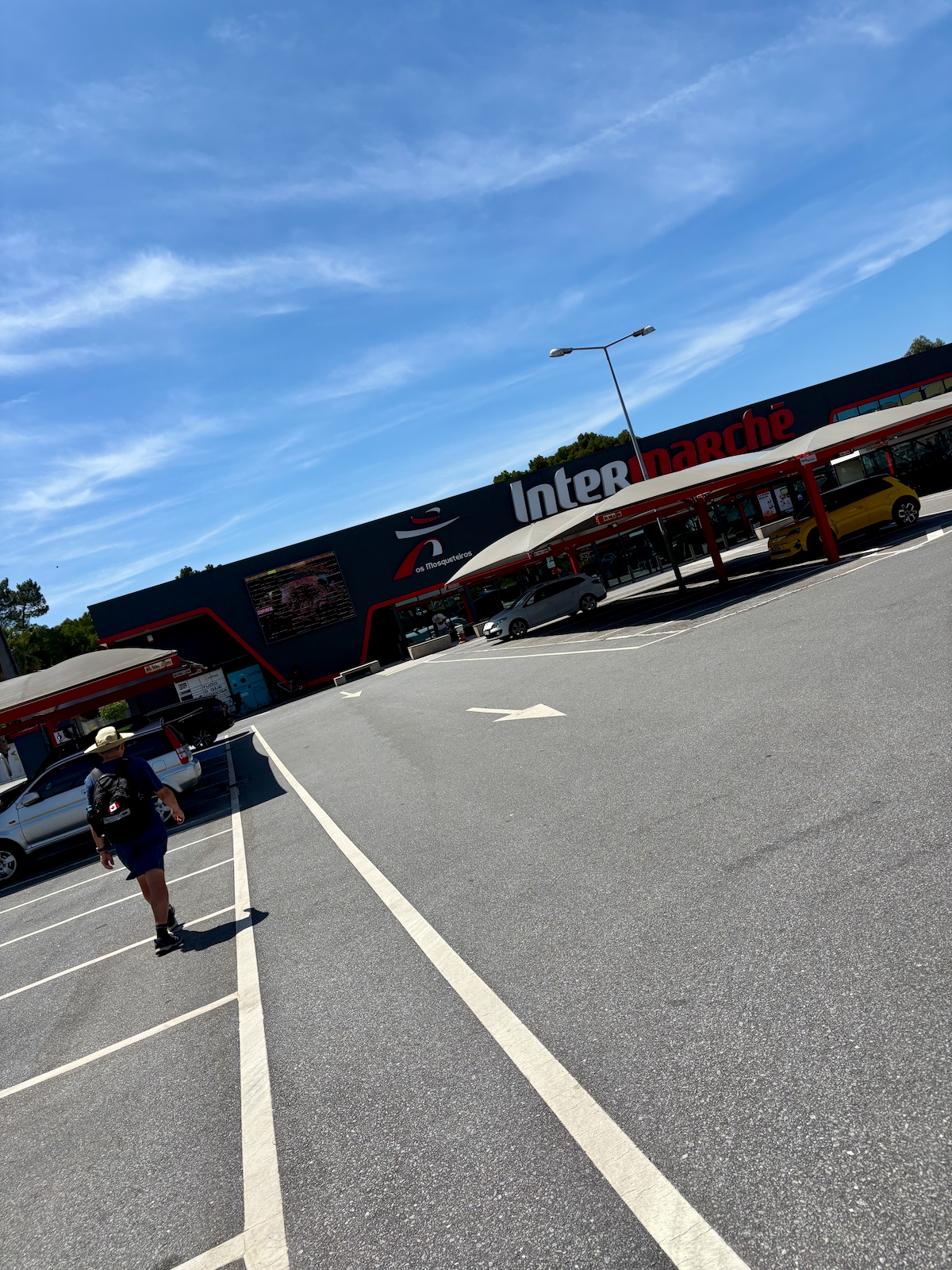 Front of Intermarché supermarket with red and blue sign; a person walks toward the entrance under a clear blue sky.