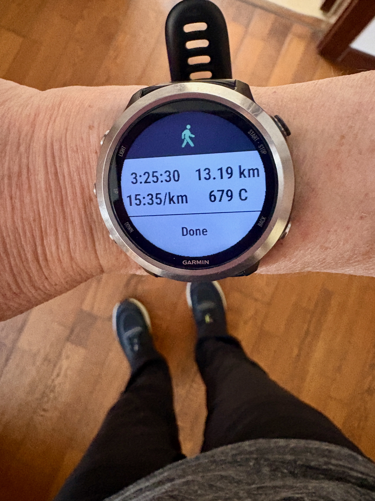 Garmin smartwatch on wrist showing a walking activity: 3:25:30 time, 13.19 km distance, 15:35/km pace, 679 kcal, with 'Done' at bottom.