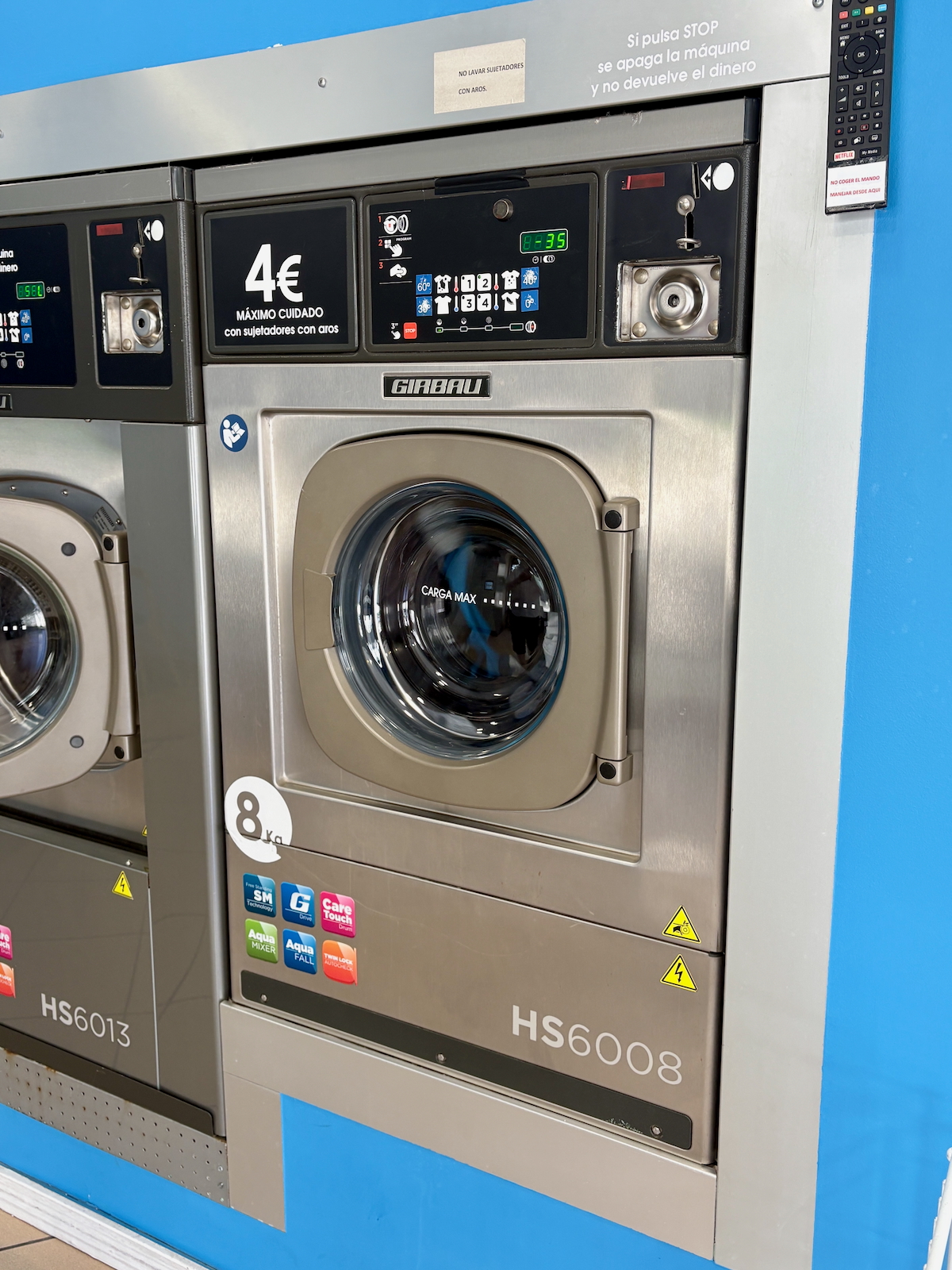 Front-loading washing machines in a laundromat, stainless steel, with blue wall and a 4€ price sign above the controls