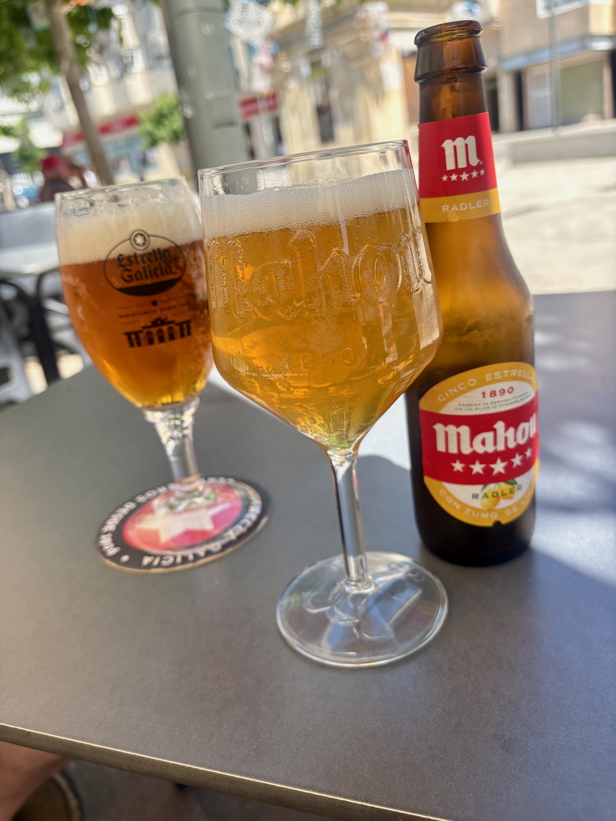 Two beers on an outdoor table, a Mahou Radler bottle beside them and a foamy glass in the foreground.