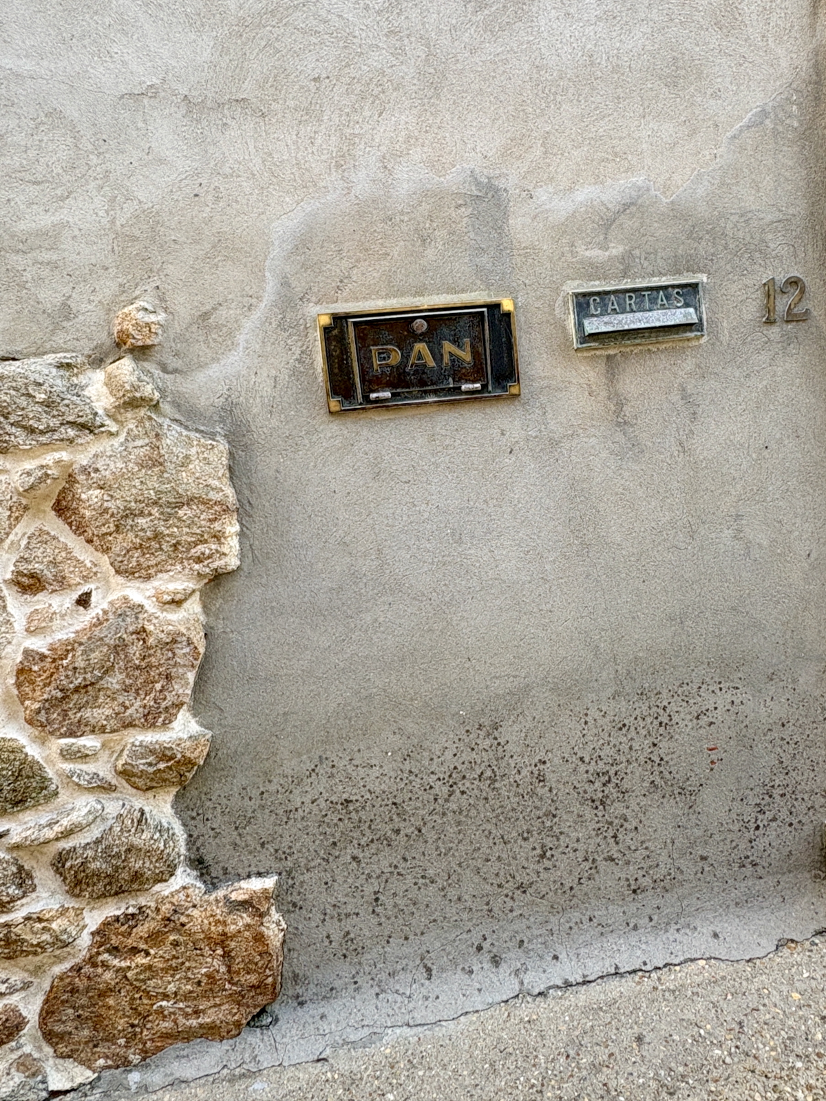 Exterior wall with a black metal mailbox labeled PAN and a separate 'CARTAS' letter slot, house number 12, beside a stone foundation.