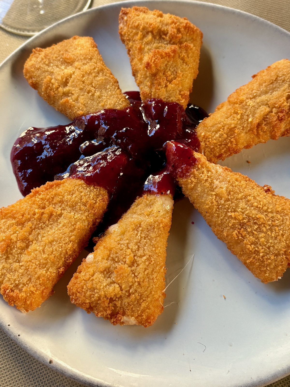 Plate of six golden fried cheese portions arranged in a circle around a pool of red berry sauce.