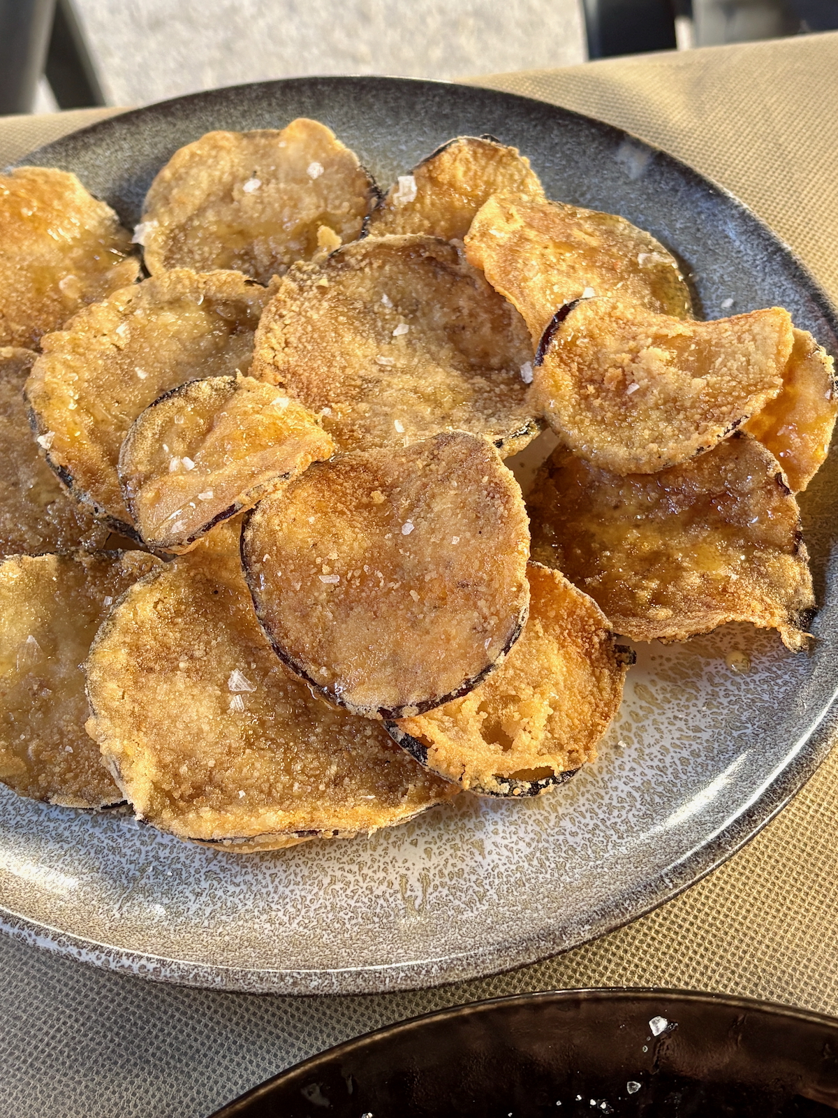 Plate of crispy fried eggplant slices sprinkled with salt.