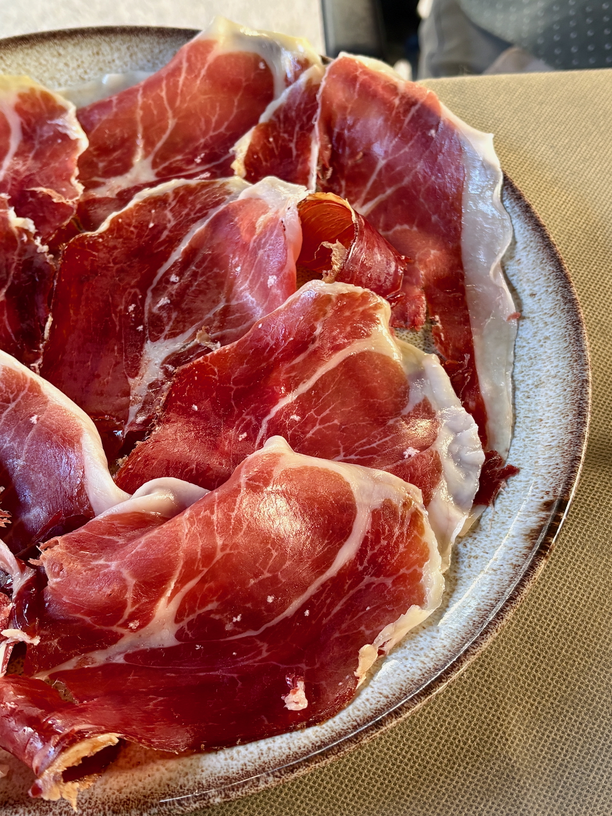 Thinly sliced cured ham with white fat marbling arranged on a ceramic plate.