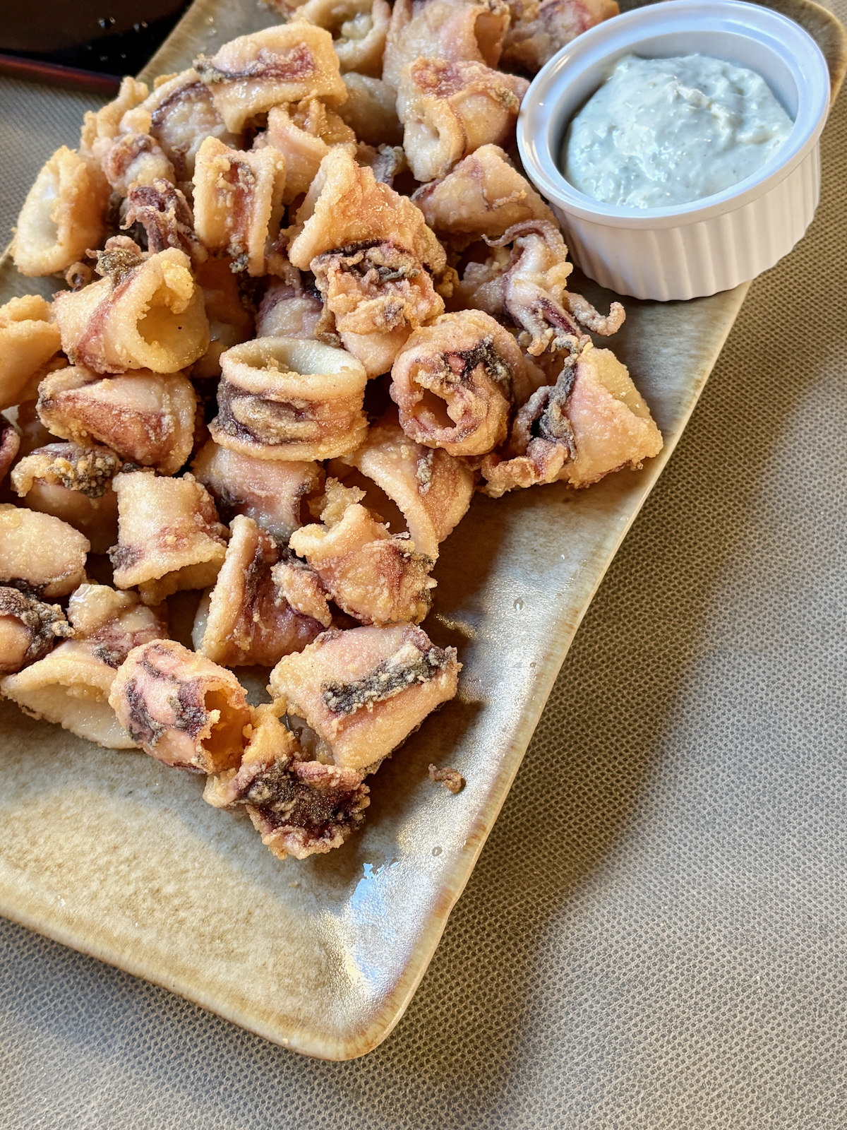 Plate of fried calamari bites with a creamy dipping sauce in a white ramekin.